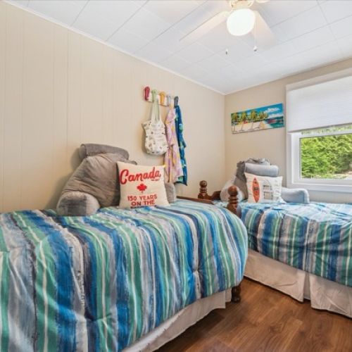Bright and cheerful bedroom with twin beds, cozy striped bedding, and a charming cottage view.