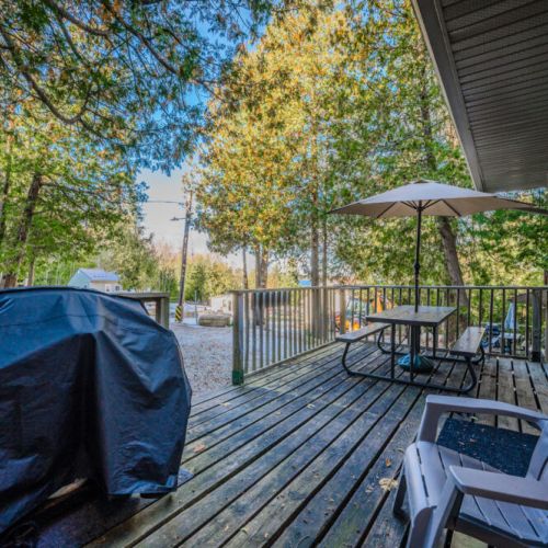 A spacious deck equipped with a BBQ grill, picnic table, and Adirondack chairs, perfect for gathering and enjoying meals outdoors.