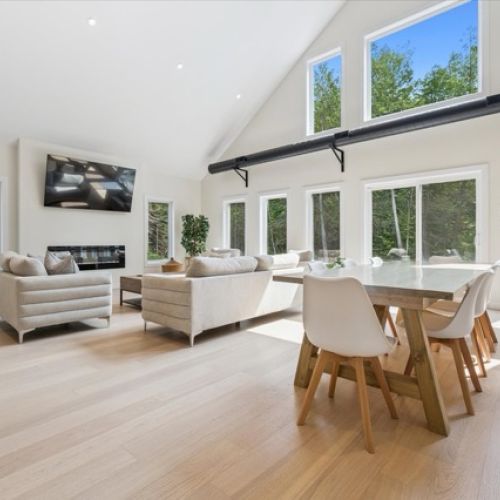 Breathtaking and bright — this open-concept great room features soaring ceilings, floor-to-ceiling windows, and seamless flow between lounging, dining, and forest views.