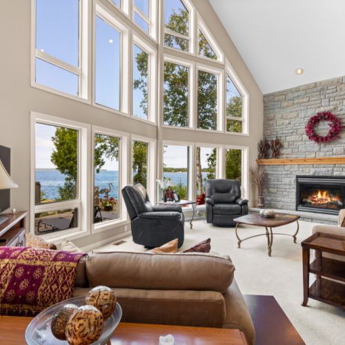 The heart of The Captain’s Lookout — a spectacular vaulted great room with a stone fireplace, comfortable seating, and walls of windows overlooking the water.