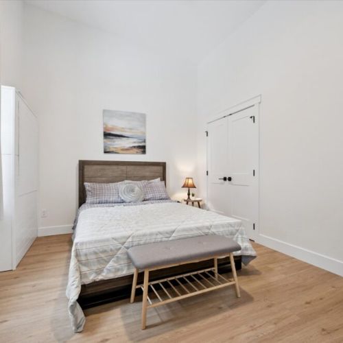 Cozy queen bedroom with minimalist décor, warm wood floors, and a calm, restful atmosphere.