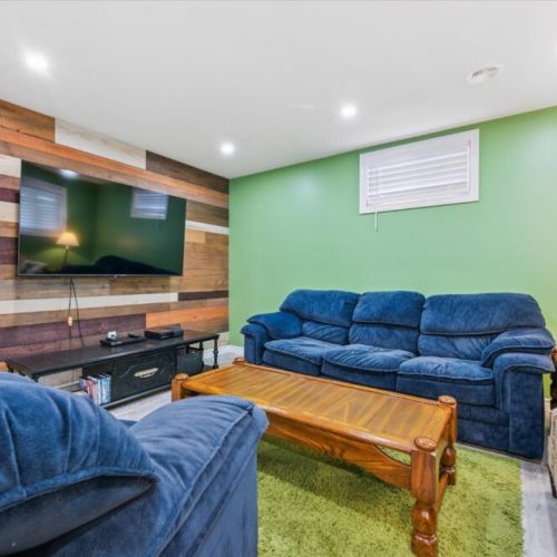 Inviting entertainment area featuring a large flat-screen TV mounted on a rustic wood accent wall, complemented by plush blue sofas and a cozy green rug—perfect for movie nights or relaxing with friends and family.