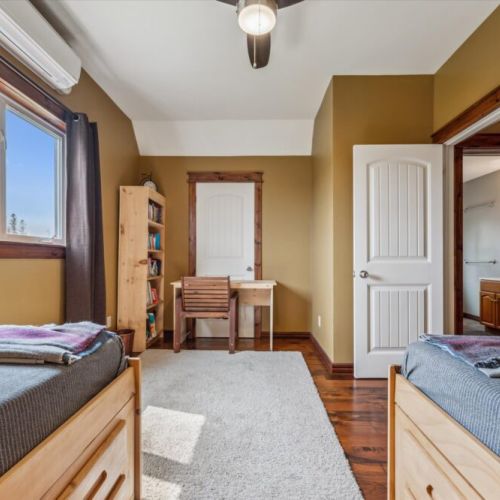 Charming upstairs twin bedroom with two single beds, built-in drawers, moose-themed pillows, and a soft carpeted play space.