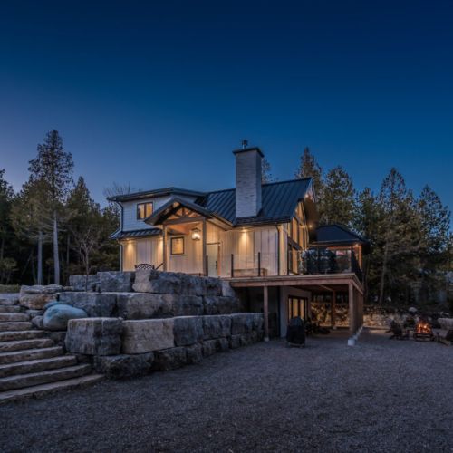 Experience cozy luxury at this vacation rental featuring a modern chalet design, dramatic stone landscaping, and a glowing fire pit—ideal for serene nature getaways and lakeside escapes.