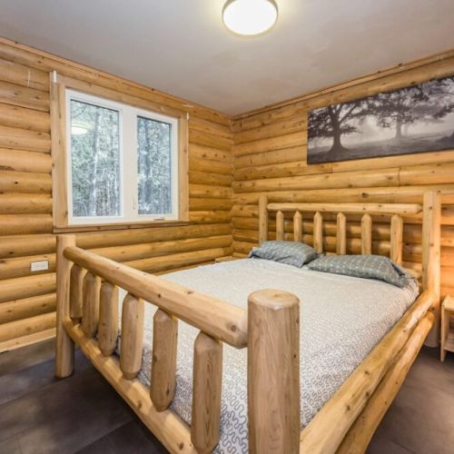 Main floor Guest bedroom that channels the forest's stillness with its log walls and simple decor, promising a restful night.