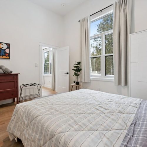 Serene bedroom retreat with queen bed, tall ceilings, and large windows overlooking the trees.