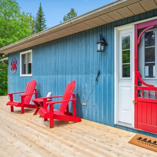 Settle into classic cottage life with vibrant red Muskoka chairs and a screen door that says it all.