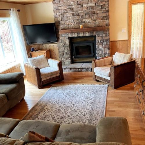 Unwind in the inviting living room with a stone fireplace, soft seating, and forest views—ideal for a cozy cottage getaway.