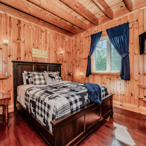 Comfortable guest room with queen bed, charming moose-themed linens, and rustic warmth—great for couples or solo travellers seeking a cozy retreat.