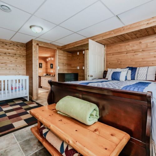 Escape to the ground level bedroom, where restful nights await. This room features natural wood furnishings, soft lighting, and a comfortable bed, all designed to create a tranquil and cozy sleeping environment. A crib is also present, great for families with young children.