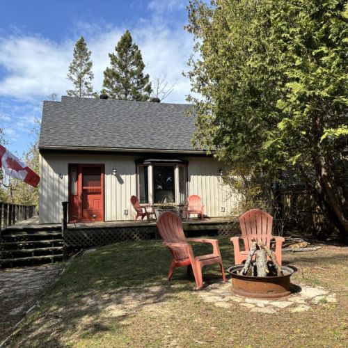 Welcoming Cottage Facade: This image captures the front view of The Louise, framed by the natural beauty of its surroundings. The red Adirondack chairs on the porch offer a warm invitation to relax and enjoy the serene atmosphere of North Oliphant Beach.