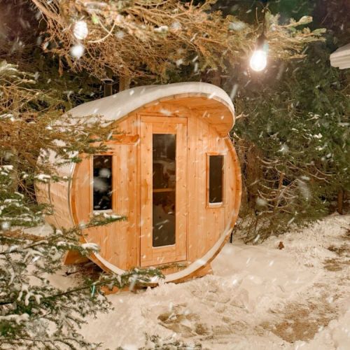 Snow swirling through the evergreens as Driftwood’s cedar barrel sauna glows softly in the winter night, a warm little retreat tucked into the quiet of fresh-fallen snow.