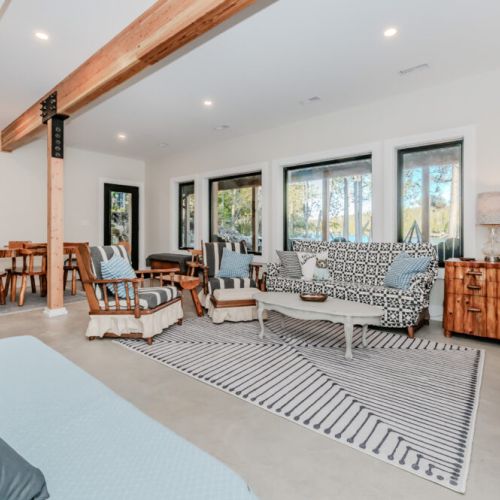 Enjoy spacious open-concept living in this charming cottage rental, complete with a bright lounge area, handcrafted wooden dining table, and expansive forest and lake views for the ultimate retreat experience.