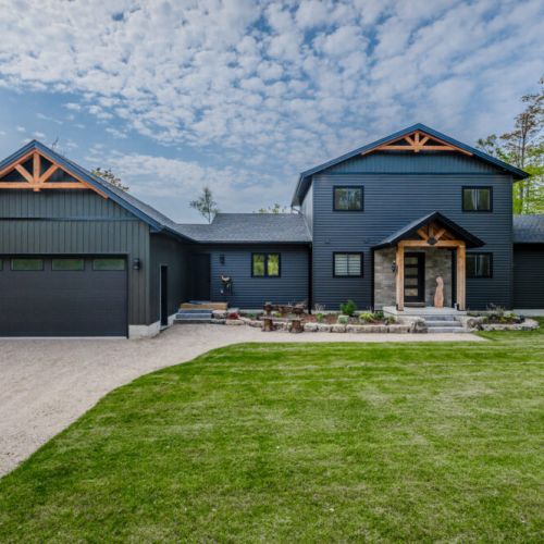 This stunning modern retreat, nestled within the serene Bruce Peninsula, offers an inviting and spacious design. The dark exterior contrasts beautifully with the lush greenery and bright sky, creating a tranquil ambiance perfect for relaxation.