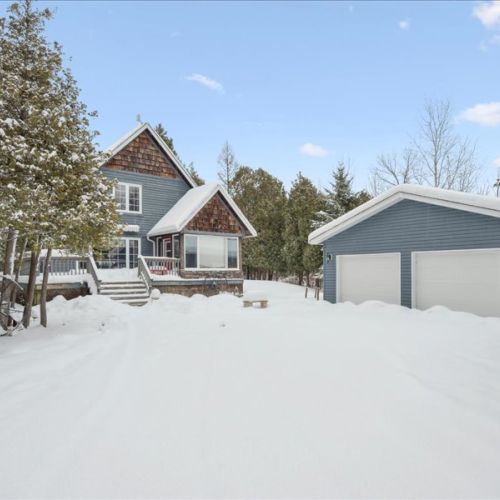 Exterior view showing the cottage and detached garage, surrounded by trees and winter beauty.