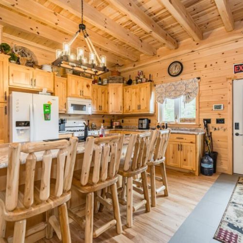 The awe-inspiring open concept kitchen, complete with a majestic island and handcrafted log bar-stools, is a hub of entertainment and warmth, inviting you to create culinary delights against the backdrop of the crackling fireplace.