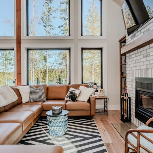 Relax in style in the spacious living room with a cozy leather sectional, panoramic forest views, and a gas fireplace—ideal for a relaxing lodge escape or lakeside vacation rental.