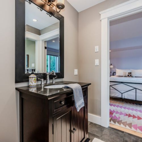 Stylish bathroom with a dark wood vanity and sleek fixtures, leading into a bright and cozy bedroom with soft tones and vibrant accents.