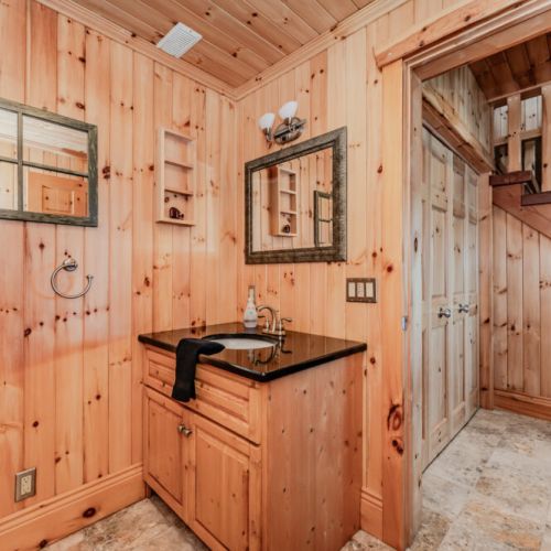 Rustic powder room with warm wood paneling, granite countertop, and cozy cabin charm—ideal for guests seeking a comfortable and authentic vacation rental experience in a peaceful, nature-filled retreat.