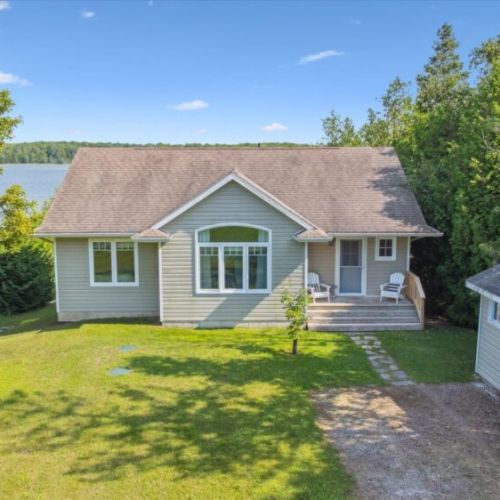 Charming lakefront cottage with a welcoming front porch, surrounded by mature trees for privacy, and offering a serene view of the water just steps from the door.