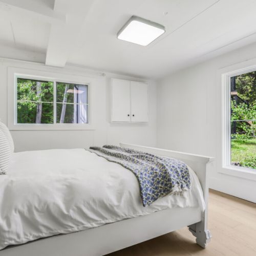 Light filled bedroom with windows on two sides and peaceful treetop views.