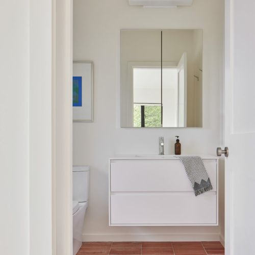 A bright bathroom with a clean, floating vanity and terracotta floor tiles.