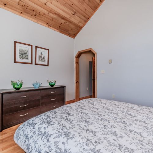 Bright bedroom with dresser and vaulted pine ceilings—your restful retreat during a nature-filled holiday escape.
