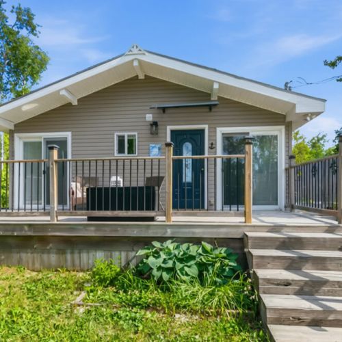 A charming cottage entrance with a welcoming deck and steps. A peaceful vacation home offering comfort, privacy, and easy outdoor living.
