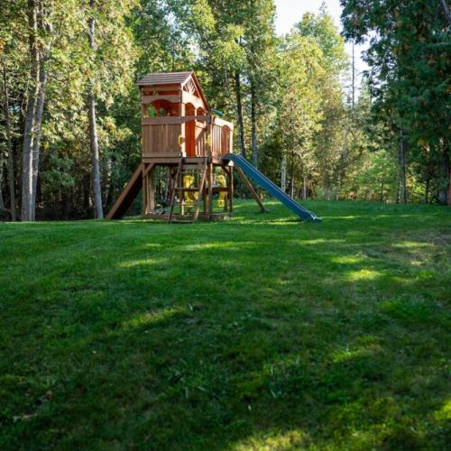 Tree house and children's toys are located at the front of the property with a large opening for family activities.