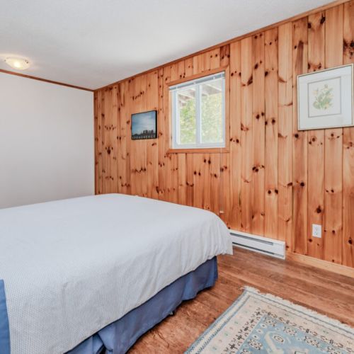 Rustic primary bedroom with wood-paneled charm, cozy bedding, and serene views — the ultimate place to unwind after lakeside adventures.