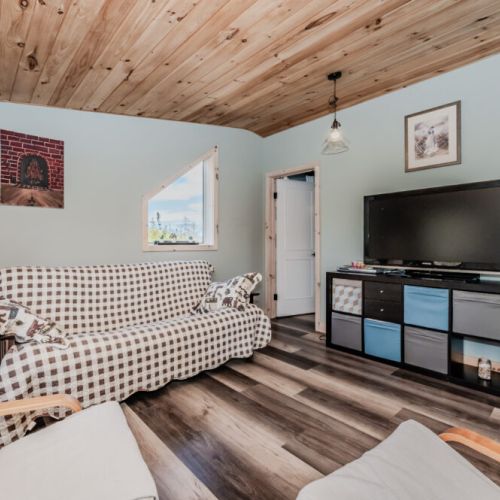 Wind down in the comfy cottage lounge with wood-paneled ceilings, cozy seating, and a TV setup—perfect for movie nights or rainy day relaxation.