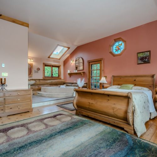 A spacious bedroom with vaulted ceilings and warm wood accents offers an inviting retreat. Natural light floods the room, creating a serene and airy atmosphere for rest and relaxation.