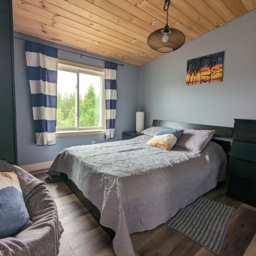 Cozy second bedroom with a comfy bed, soft lighting, and peaceful forest views—perfect for restful mornings in nature.