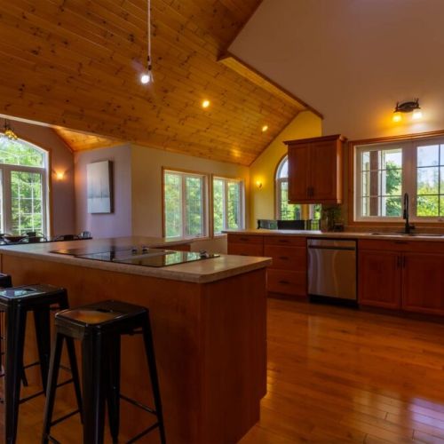 Cook and connect in a spacious open-concept kitchen with vaulted ceilings, large windows, and forest views—perfect for group stays and gatherings.