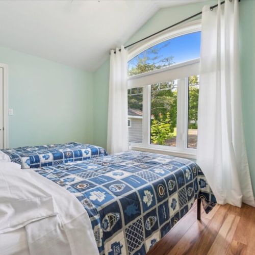 Bright bedroom with twin beds, vaulted ceiling, and large window bringing in plenty of natural light — plus playful hockey-themed bedding for fans.