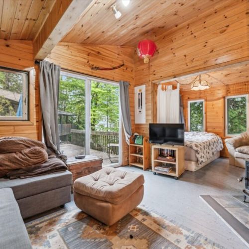 This open-concept living space connects seamlessly to the outdoors via a sliding glass door. Relax by the stove, catch a movie, or retreat to the sleeping nook — all in one cozy, sunlit space.
