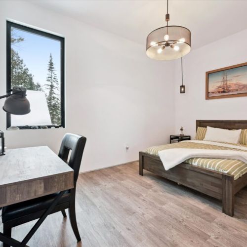 A bright bedroom featuring a dedicated desk, forest views, and a simple, calming design that feels both functional and restful.