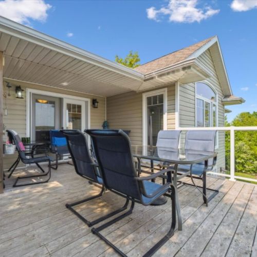 Expansive deck with glass railing, comfortable outdoor dining set, and partial cover for shade, offering a perfect blend of sun and shelter while enjoying the beautiful treetop and lake views.