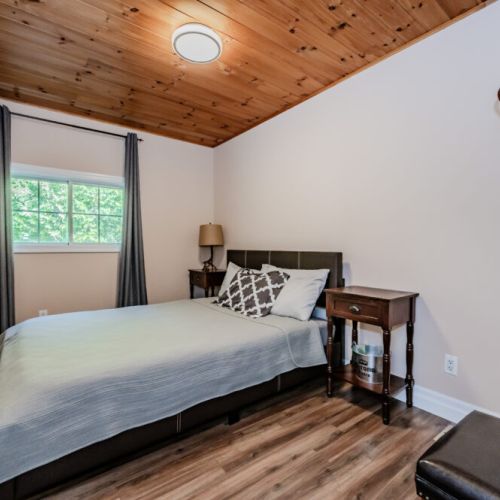 A bright and cozy guest bedroom with a queen-sized bed, ideal for a good night's sleep. The wood-paneled ceiling enhances the cozy, cottage feel.