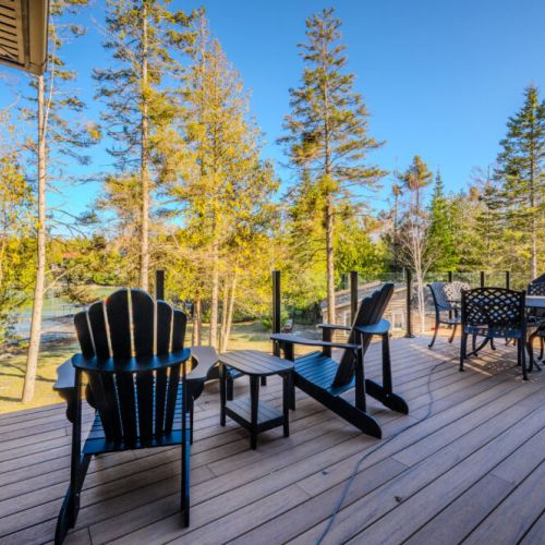 Elevated deck with Adirondack chairs and outdoor dining area, perfect for vacation relaxation, BBQ nights, and enjoying scenic lake and forest views at this stunning cottage rental.