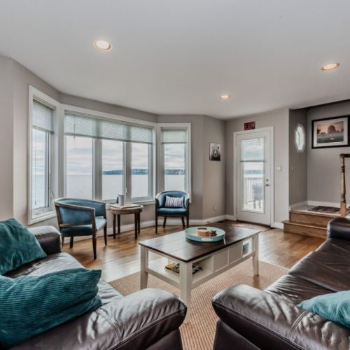 Gather in the cozy family living area featuring large windows that frame expansive views of Georgian Bay. The perfect space to unwind after exploring the Bruce Peninsula, with natural light and serene waterfront vibes.