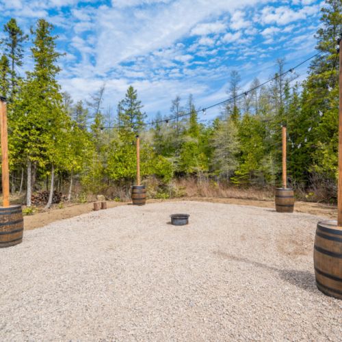 The spacious outdoor fire pit area, surrounded by woodland, is perfect for evening gatherings under the stars, enhanced by the warm glow of string lights.