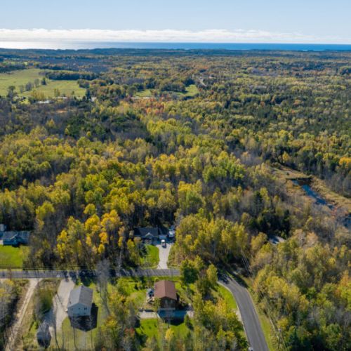 A broader aerial view of the surrounding landscape, showing the mix of open fields, forests, and distant lake views. Black Bear Cottage is perfectly situated for guests looking to immerse themselves in nature while still being close to local amenities and attractions.