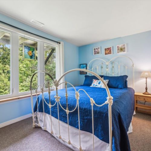 This light and airy bedroom includes a classic iron bed frame and large windows with forest views.