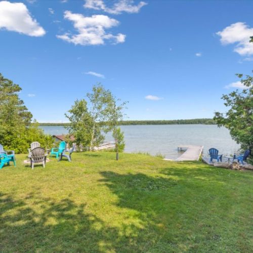 Expansive backyard with multiple seating areas, perfect for lakeside relaxation, featuring a private dock and unobstructed views of the serene water.