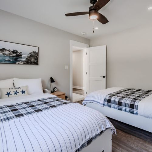 This guest bedroom features two double beds with stylish bedding, a ceiling fan, and nature-inspired artwork. It's a cozy space for additional guests.