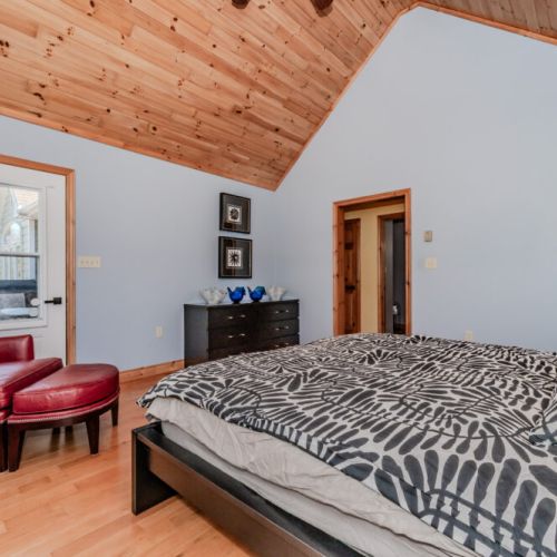 Relax in a bright king bedroom with vaulted pine ceilings, designer bedding, and private deck access – perfect for a peaceful nature retreat.