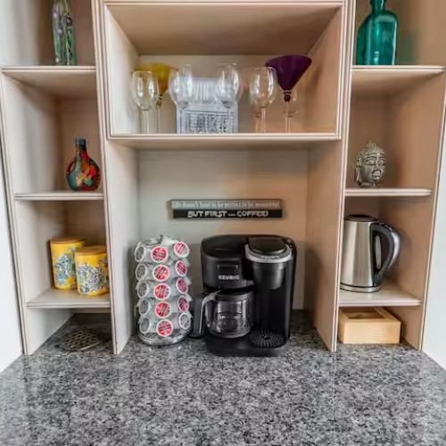 Fully stocked coffee and beverage station with a Keurig, drip coffee maker, kettle, and glassware for guests.