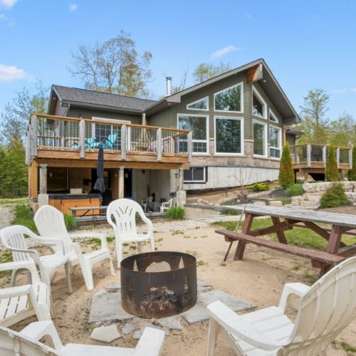 A sandy fire pit area creates a beach-like atmosphere, offering the perfect place to unwind, with six outdoor chairs gathered around the fire for relaxing evenings under the stars.