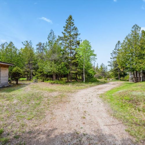 Surrounded by lush evergreens, the property features a private drive and forested setting — offering seclusion, nature views, and direct access to shoreline trails.
